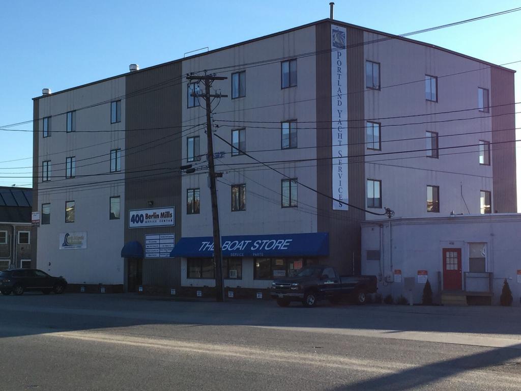 A four-story building with "Portland Yacht Services" signage, featuring businesses like "The Boat Store" and "400 Baxter Mills" on the ground floor. The structure is in an industrial area with a parked truck nearby.