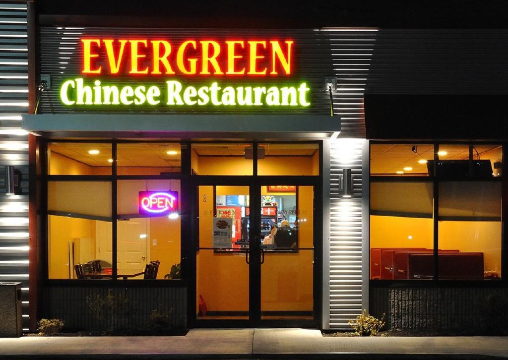 The image shows the entrance of Evergreen Chinese Restaurant at night, with a bright neon sign displaying its name. The glass door is illuminated by an "Open" sign, and the interior appears warmly lit.