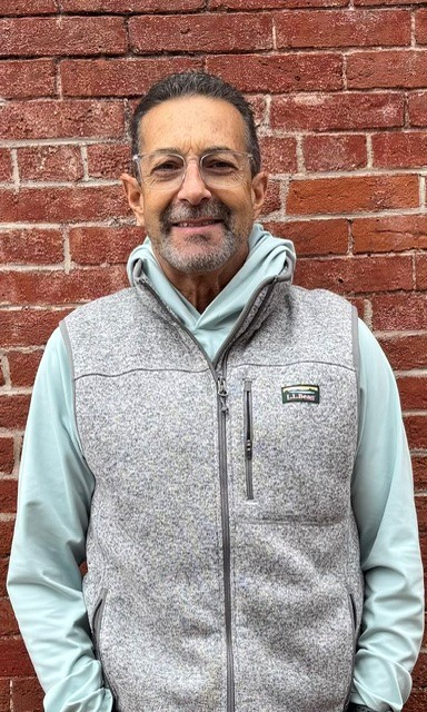 A photo of Kirk Moran, who works for Bibeau and Company, in front of a brick wall in Portland, Maine